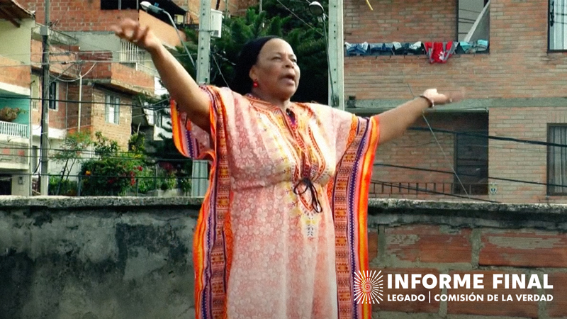 Socorro Mosquera hablando enérgicamente con sus brazos en alto, portando vestido colorido