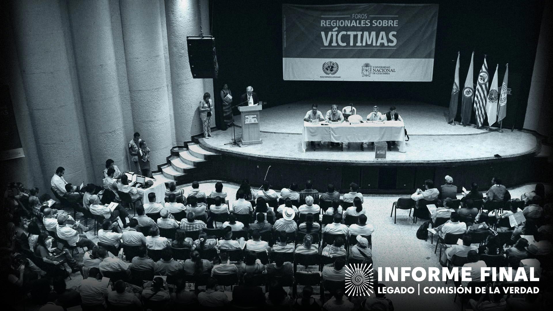 Escenario con personas que presentan a otras que están sentadas en sillas, al fondo una pancarta que dice: Foros Regionales sobre víctimas