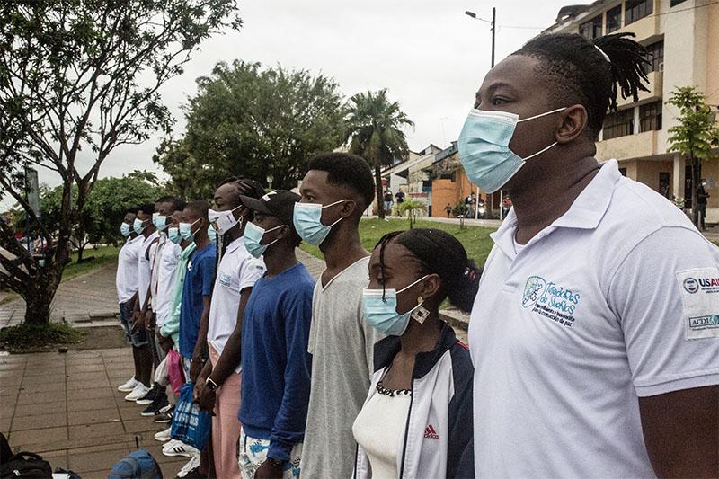 jóvenes afro con tapabocas están de pie unos junto a otros de perfil mirando al frente